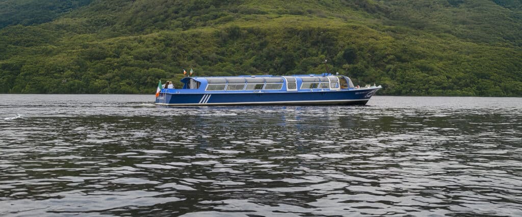 A blue tour boat on a lake surrounded by green hills.