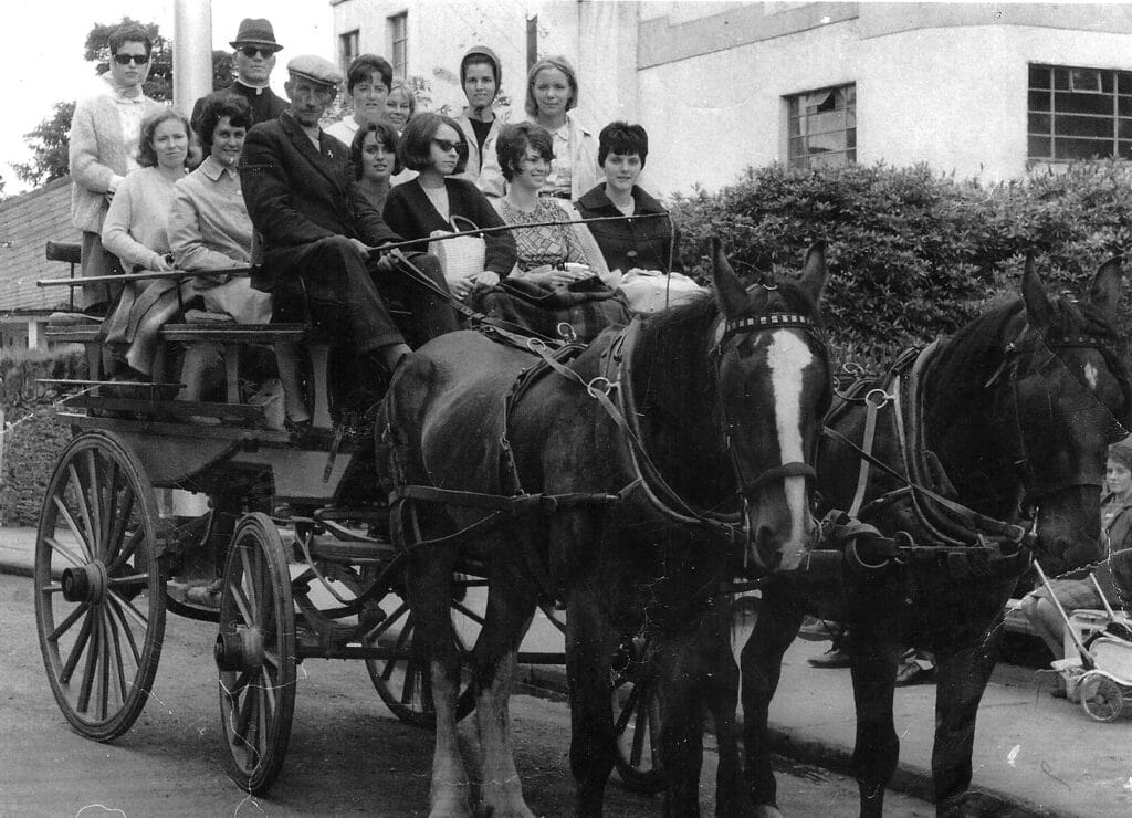 A group of people sitting in a horse-drawn carriage on a street.