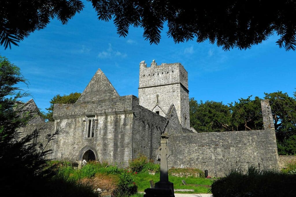 Stone abbey with tower, framed by trees against a blue sky.