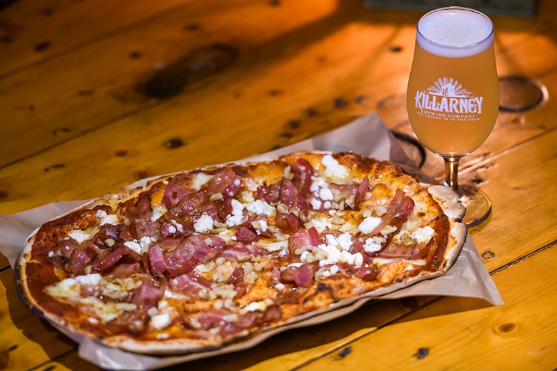 Pizza with bacon and cheese on a wooden table, next to a glass of beer.