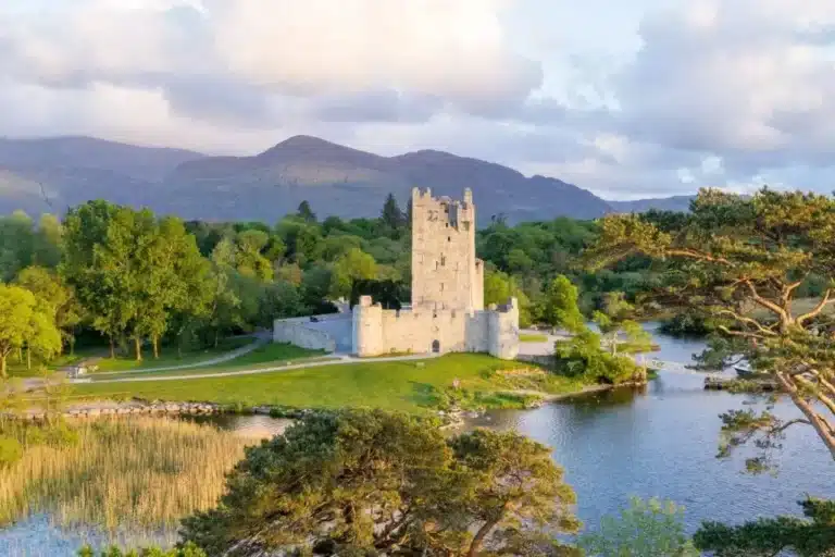 Aerial view of a stone castle beside a lake with mountains in the background.