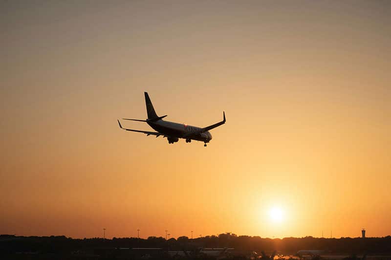 Airplane landing at sunset with a vibrant orange sky.