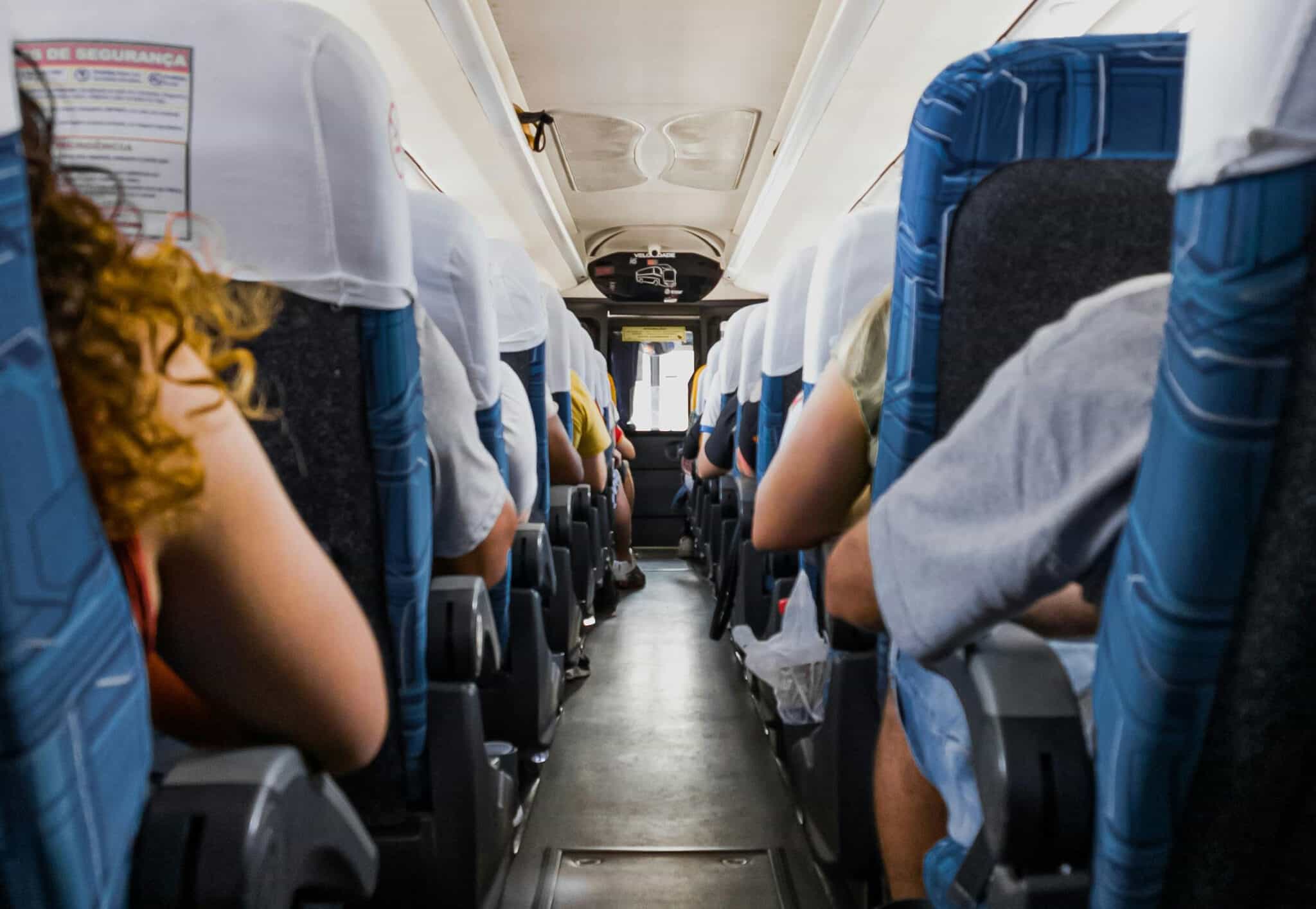 Bus interior view; passengers seated, aisle down the center.