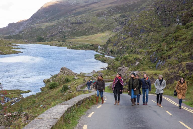 A group of people walking on a road near a lake and mountains.